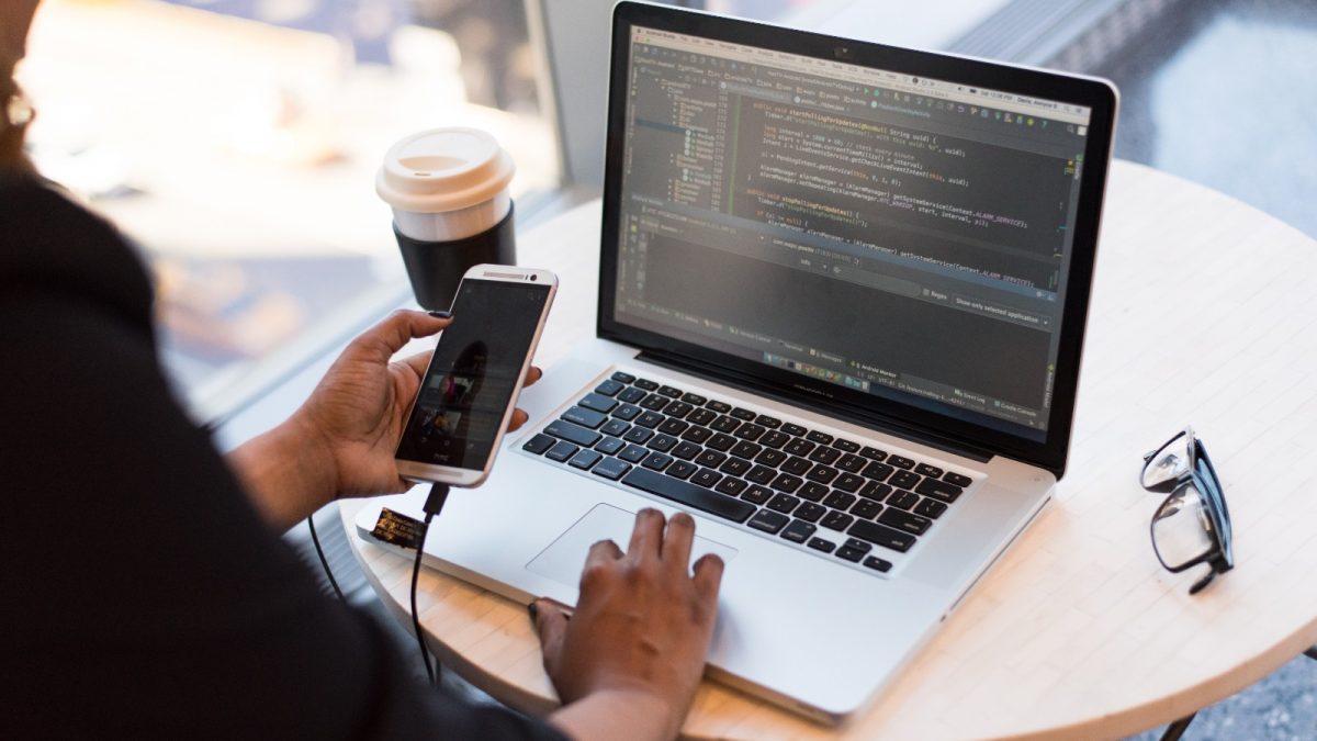 Person, die sich ein Macbook ansieht, während sie ihr Mobiltelefon verwendet