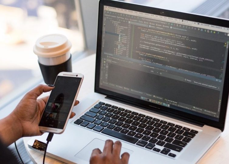 Person, die sich ein Macbook ansieht, während sie ihr Mobiltelefon verwendet