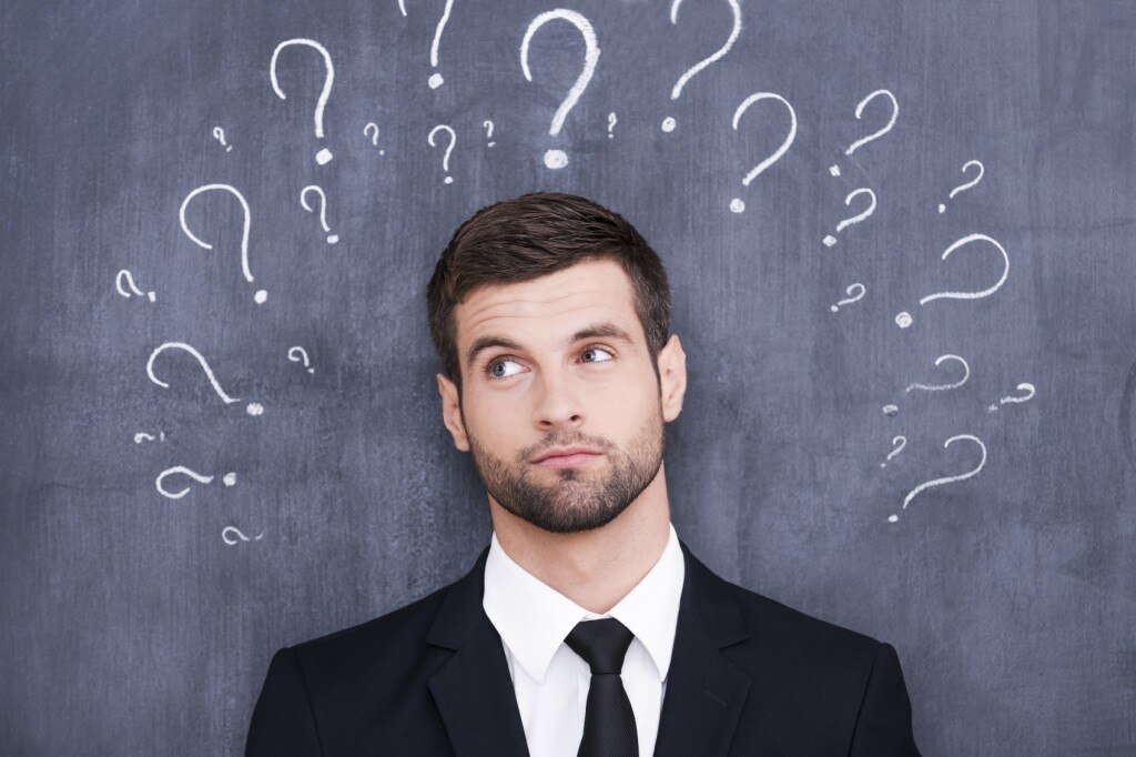 Man in suit against chalkboard with many question marks