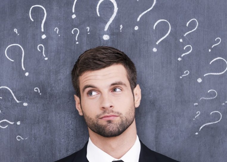 Man in suit against chalkboard with many question marks
