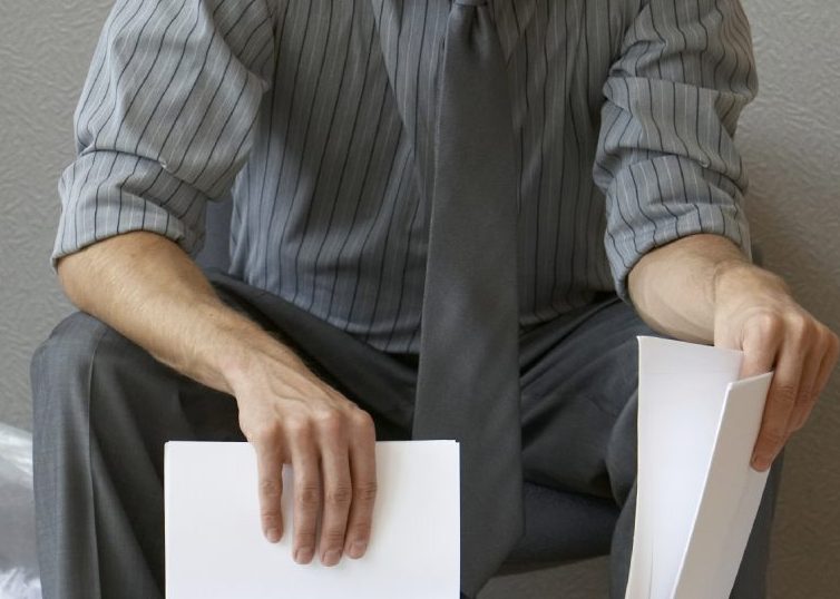 Man putting paper in a shredded with a bag full of shredded papers behind him