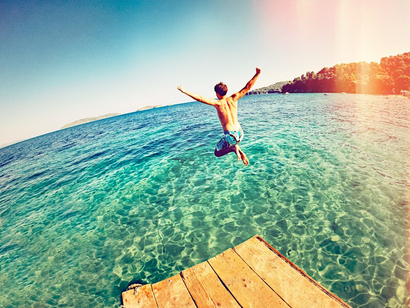 Boy jumping off a dock into the ocean