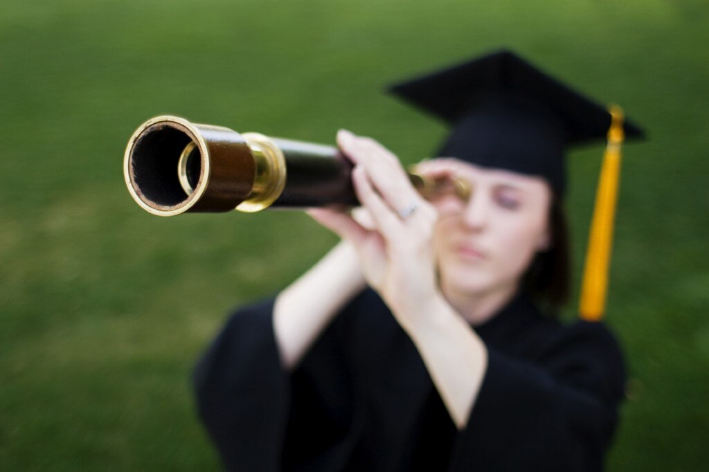 Student in graduation cap and gown looking through telescope