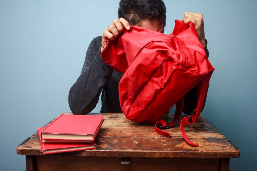 Someone sitting at a student desk with two red books on it looking into a red backpack