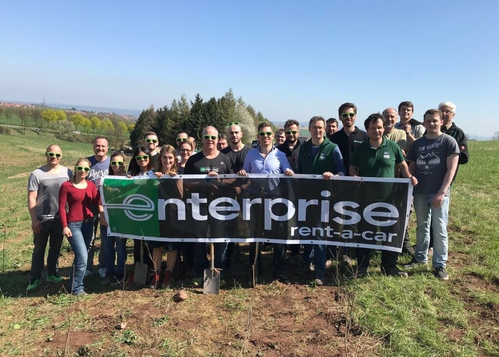 Enterprise Employees with shovels holding an Enterprise banner in a forest 
