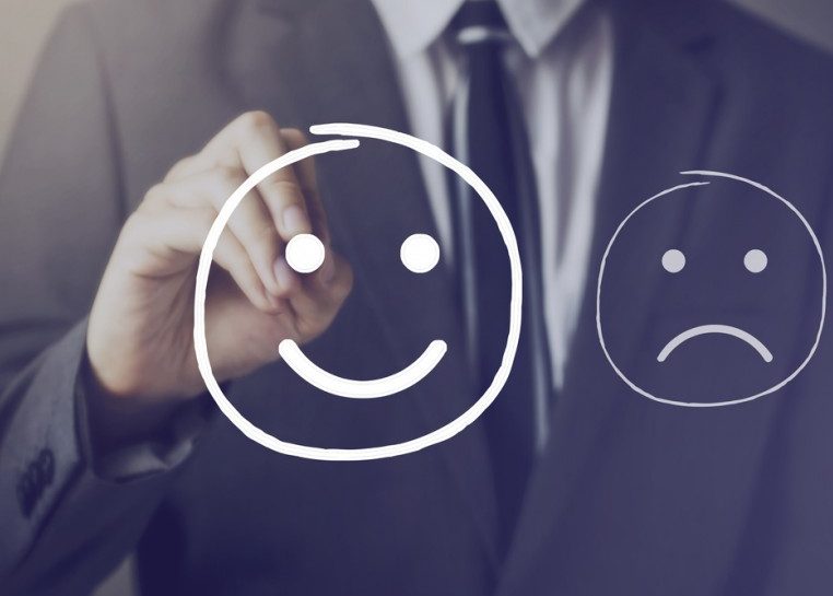 Man in suit and tie drawing a smiley face next to a frowny face