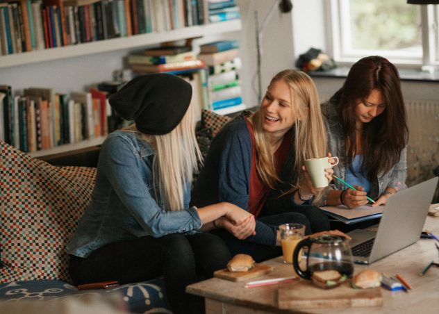 Three girls sitting on a couch together laughing and talking