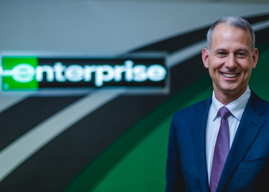 Professional photo of a man in a suit and tie in front of Enterprise signage