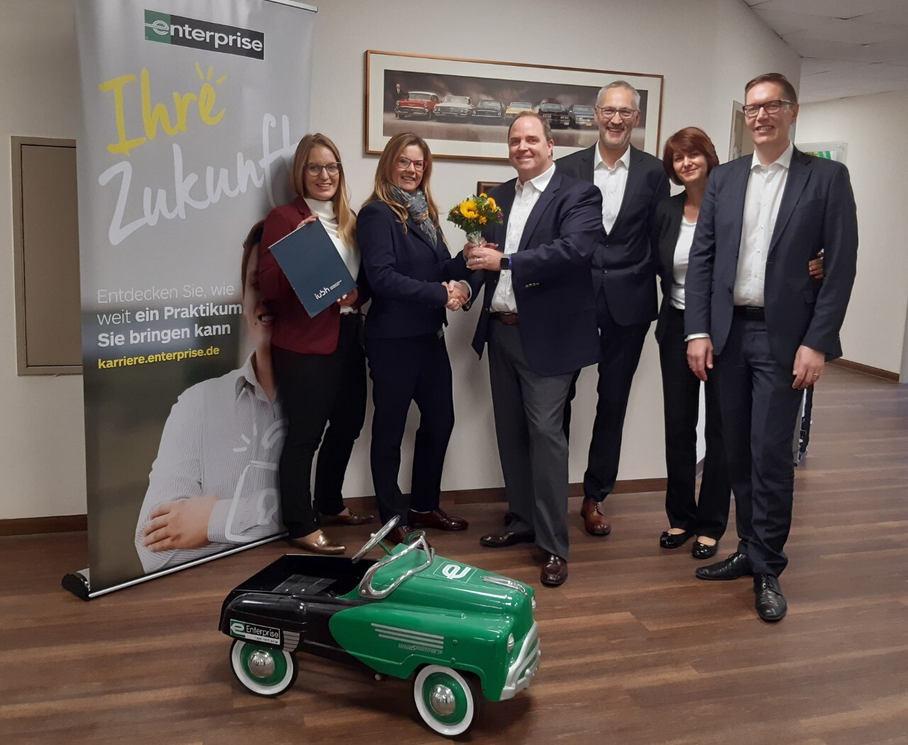 Employees in suits with flowers and a small car