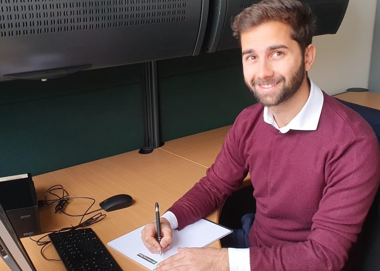 Man sitting at desk with computer while writing on a notepad