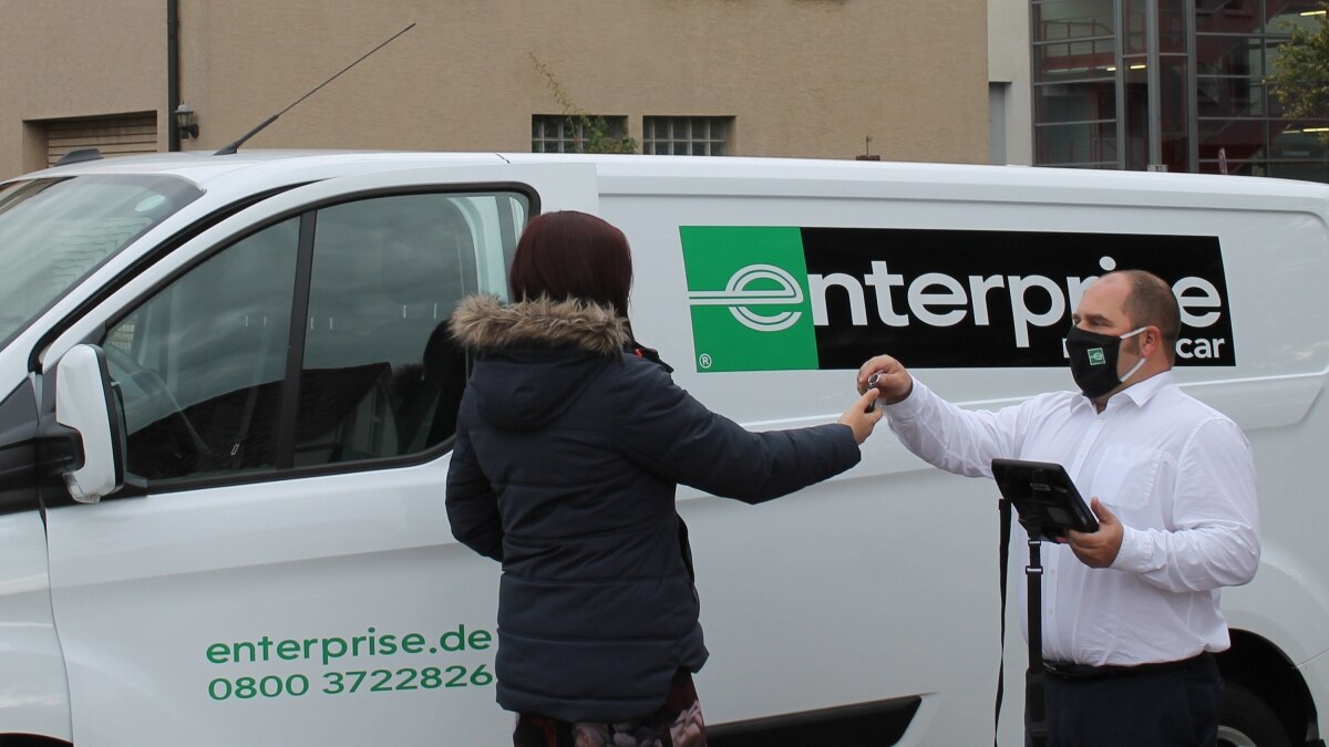 Man wearing mask handing keys to a woman in a coat in front of a moving van