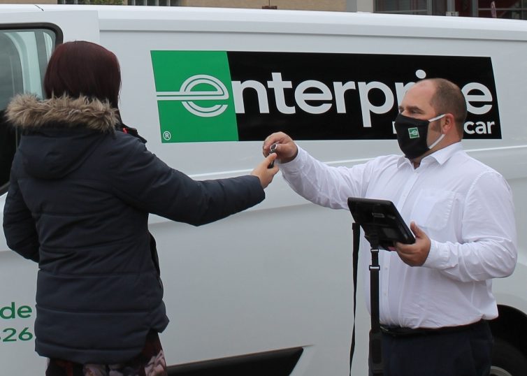 Man wearing mask handing keys to a woman in a coat in front of a moving van