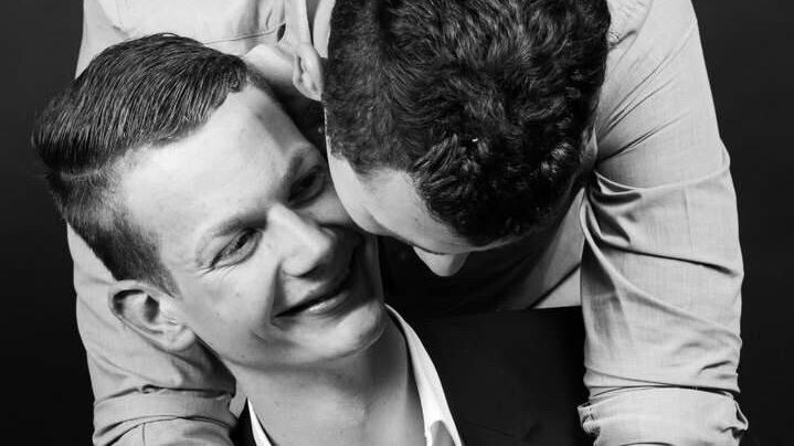 A man in a suit being embraced by another man from behind