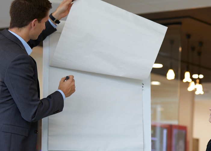 Man using flip chart in meeting while two women watch