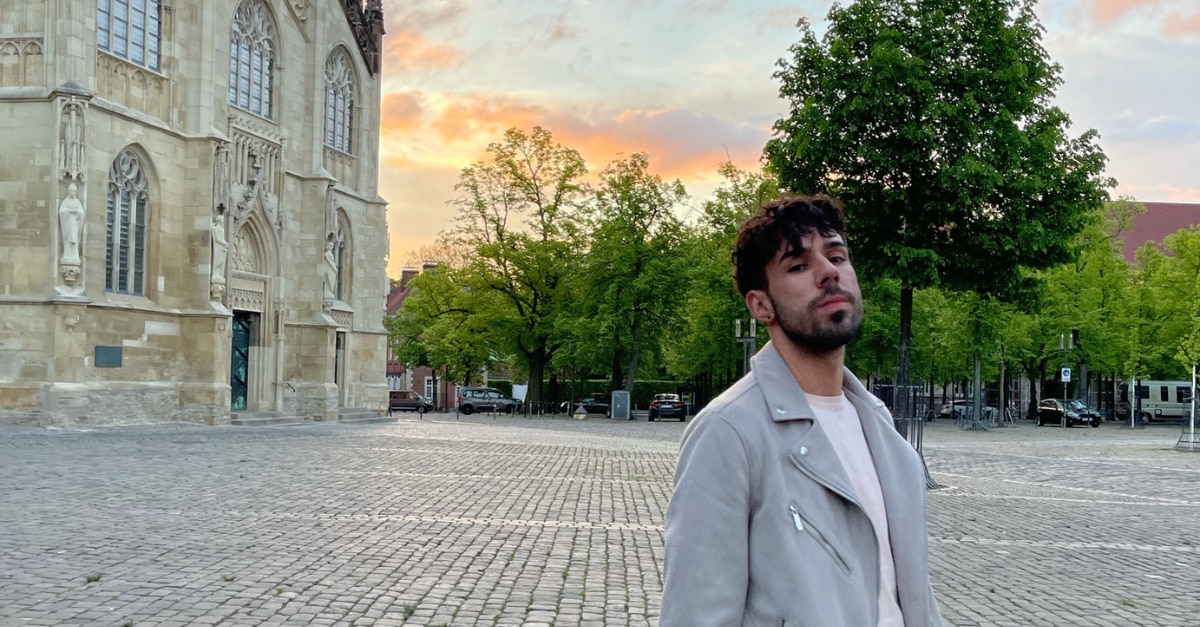 Photo of a man on a brick pathway with a church and trees behind him