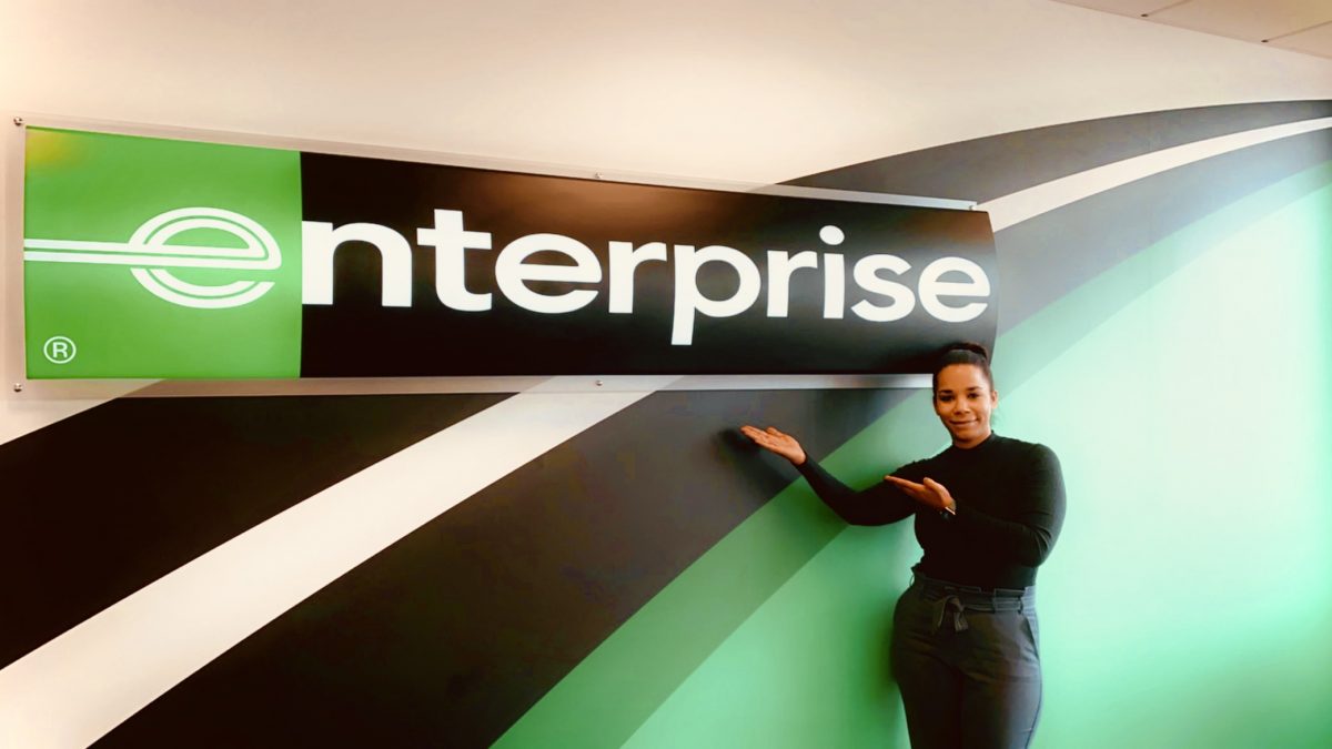 Girl wearing all black outfit showing off Enterprise sign on a wall