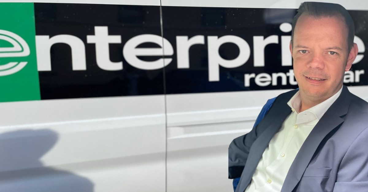 Man in suit posing in front of Enterprise van