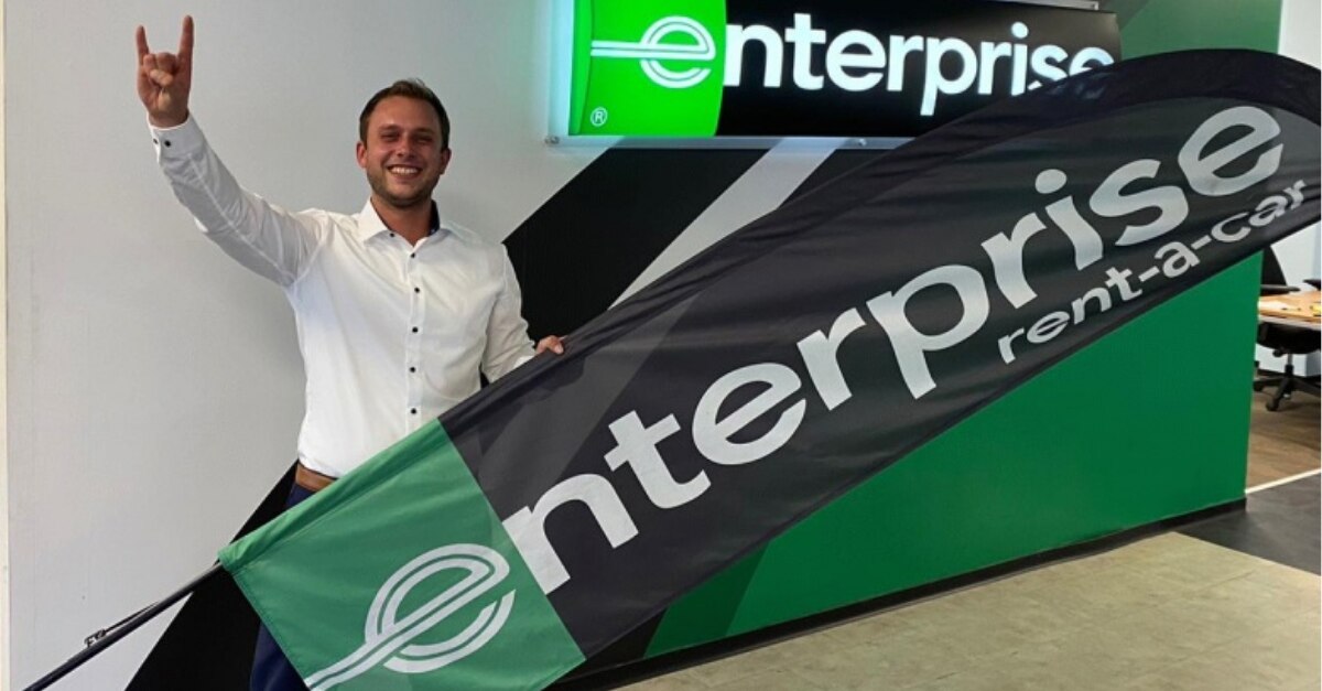 Man in white dress shirt holding an Enterprise flag with hand in the "rock and roll" sign