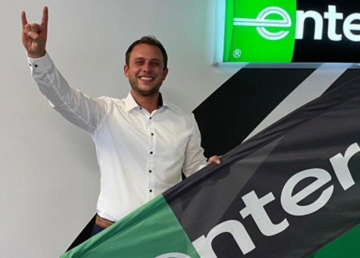 Man in white dress shirt holding an Enterprise flag with hand in the "rock and roll" sign