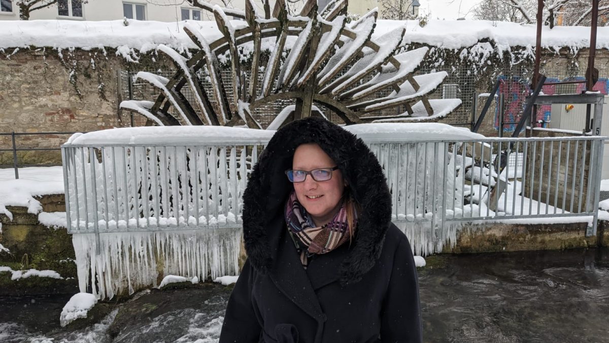 Woman in hooded coat standing in front of snow covered wheel