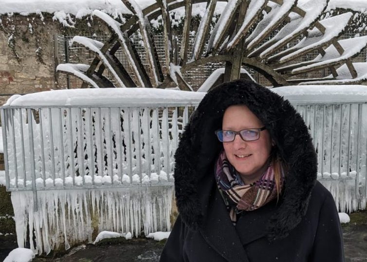 Woman in hooded coat standing in front of snow covered wheel