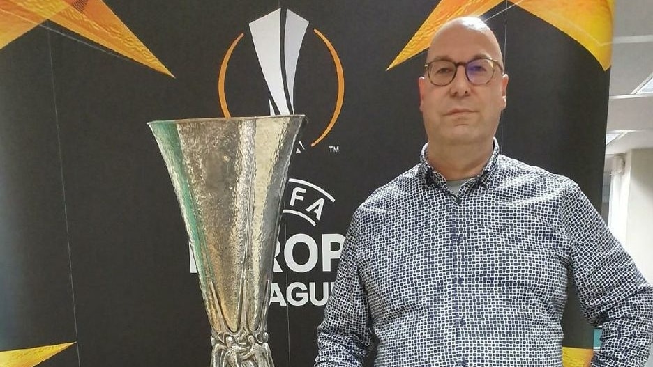 Man with glasses in patterned dress shirt standing next to a trophy