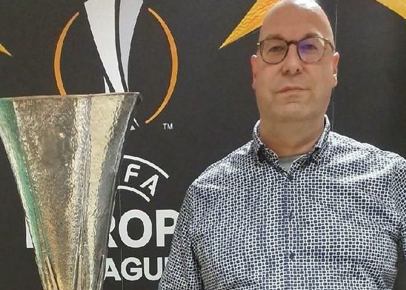 Man with glasses in patterned dress shirt standing next to a trophy