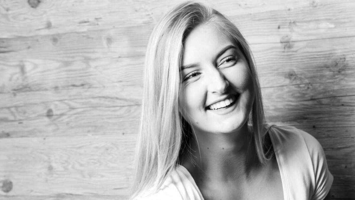 Black and white photo of girl smiling in front of wood wall
