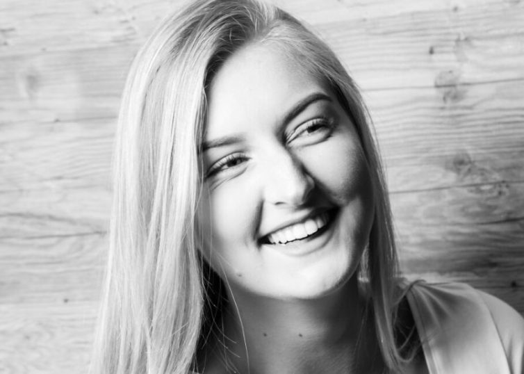 Black and white photo of girl smiling in front of wood wall