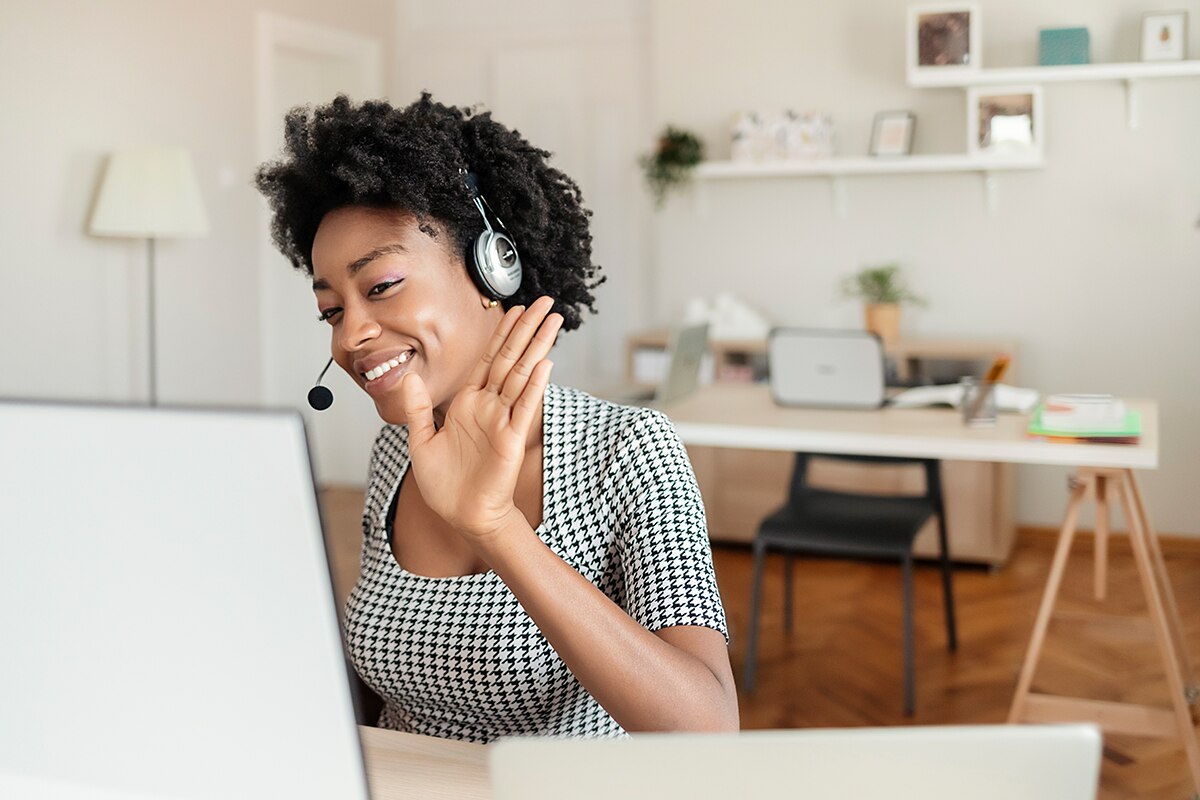 Girl wearing headset and waving to the camera on her computer