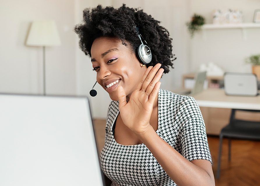 Girl wearing headset and waving to the camera on her computer