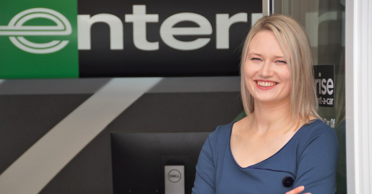 Woman leaning against door with Enterprise sign in background