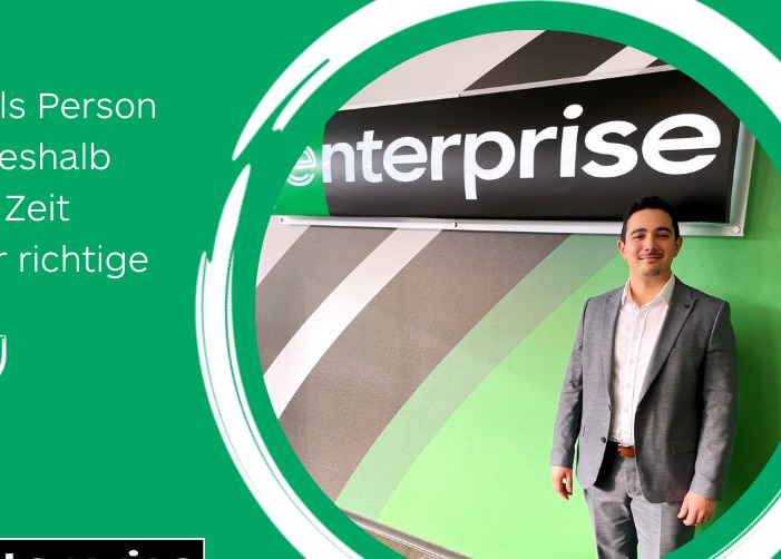 Man in grey suit standing in front of Enterprise sign with a quote on a green background