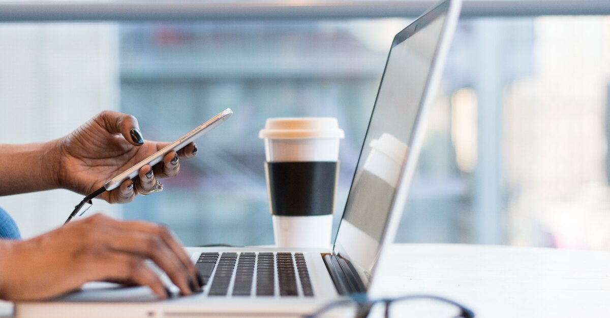 Hands typing on an open laptop and using a cellphone