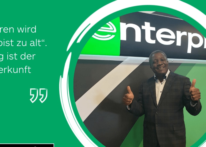 Man in suit giving two thumbs up in front of Enterprise sign with quote on green background