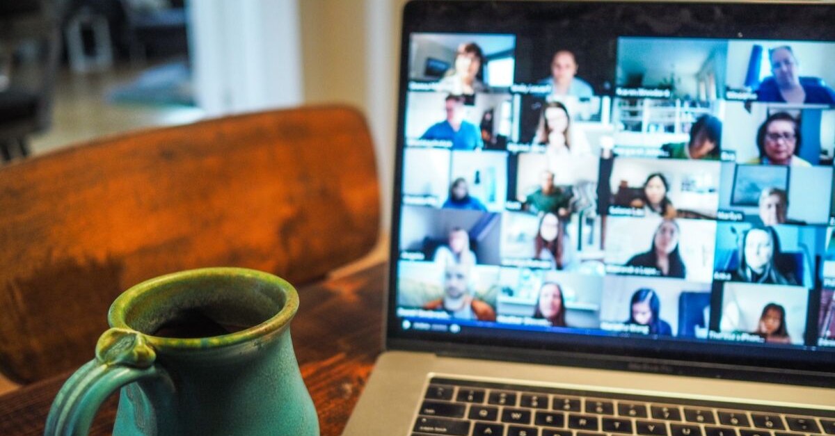 Open Macbook with Zoom meeting on screen sitting on table next to green mug