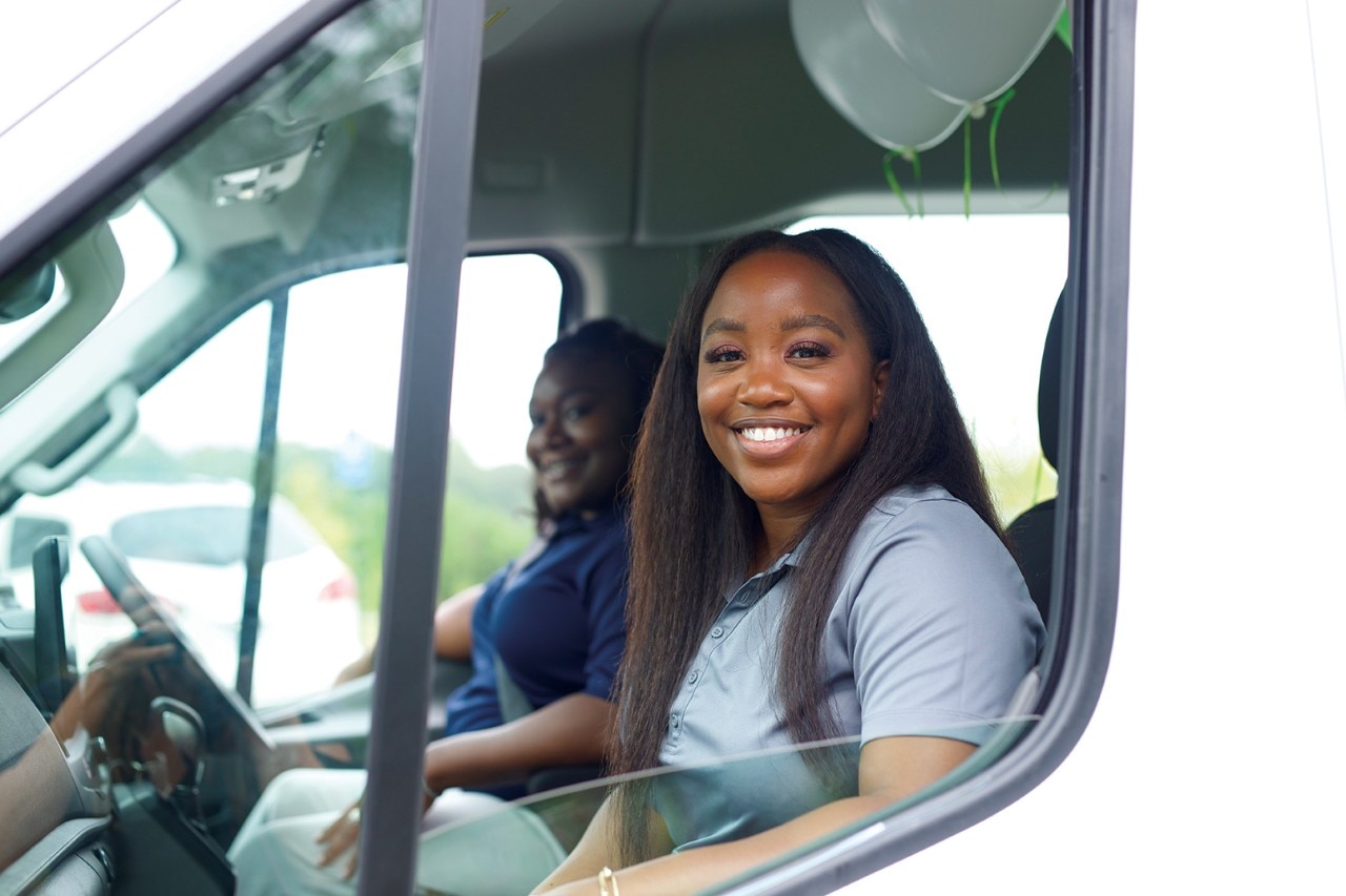 Two Enterprise Mobility team members driving a van at a local neighborhood retail branch office. 