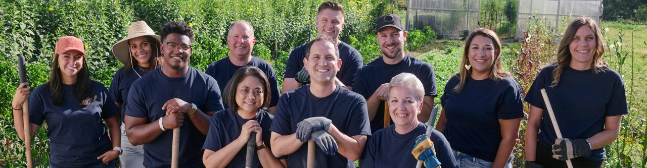 Eine Gruppe lächelnder Teammitglieder von Enterprise Mobility mit Schaufeln und Harken auf einem sonnigen Feld 