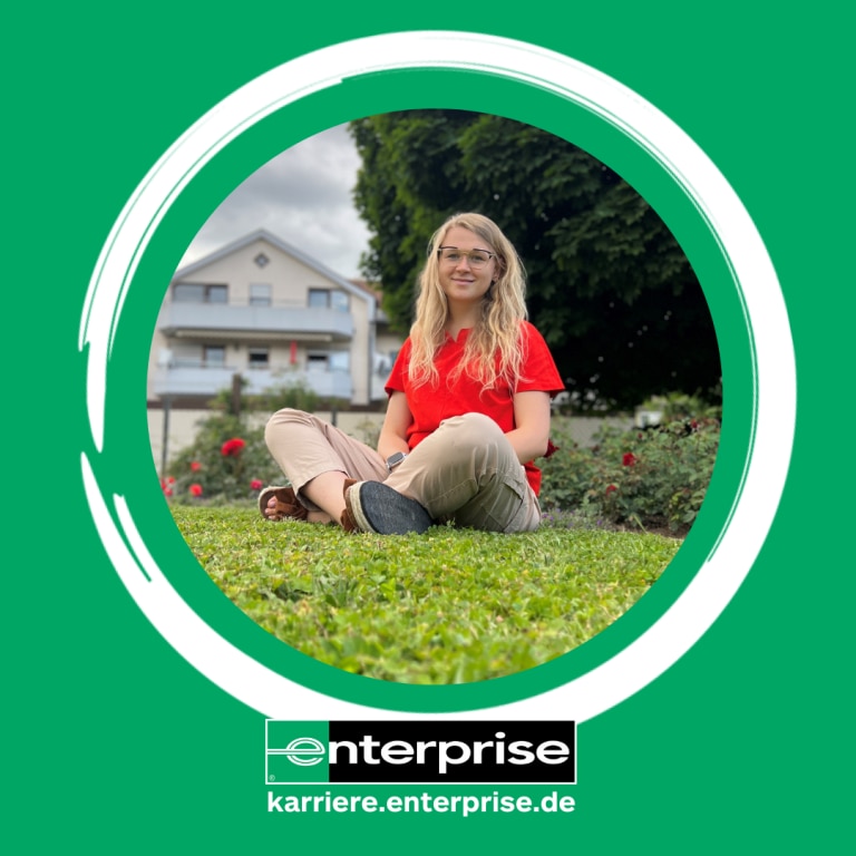 Girl in red shirt sitting in grass with a house in the background